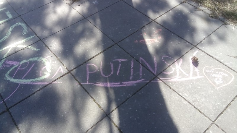 Scritta infantile in gessetto rosa su pavimentazione grigia: «PÍČA PUTINSKÁ».