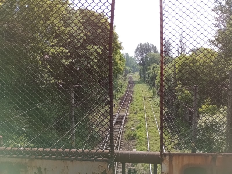 Linea ferroviaria a binario unico dall’aspetto dimesso vista da un cavalcavia con vecchie griglie di ferro.