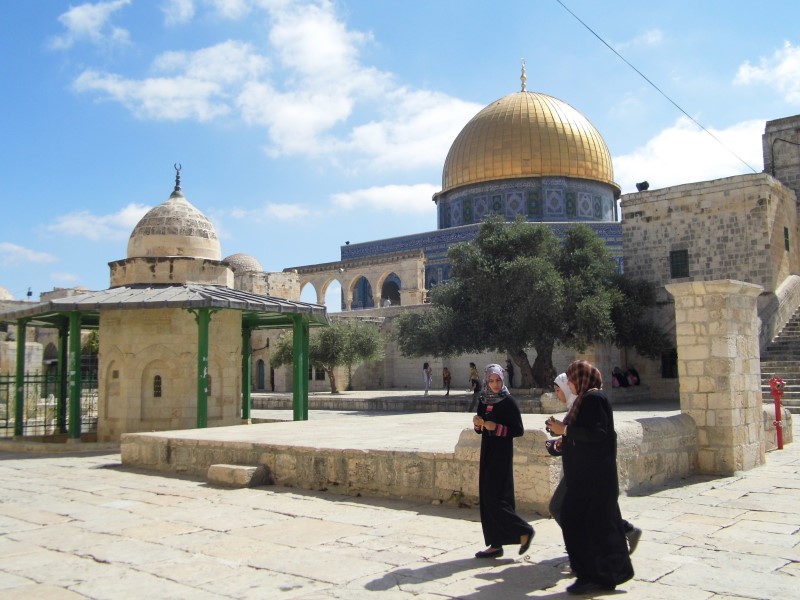 Three young Muslim women walking on Haram ash-Sharif, talking with one another, with the Dome of the Rock in the background.