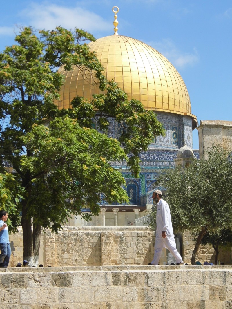 The Dome of the Rock as seen among trees, with a child and an adult man in a white robe in the foreground.